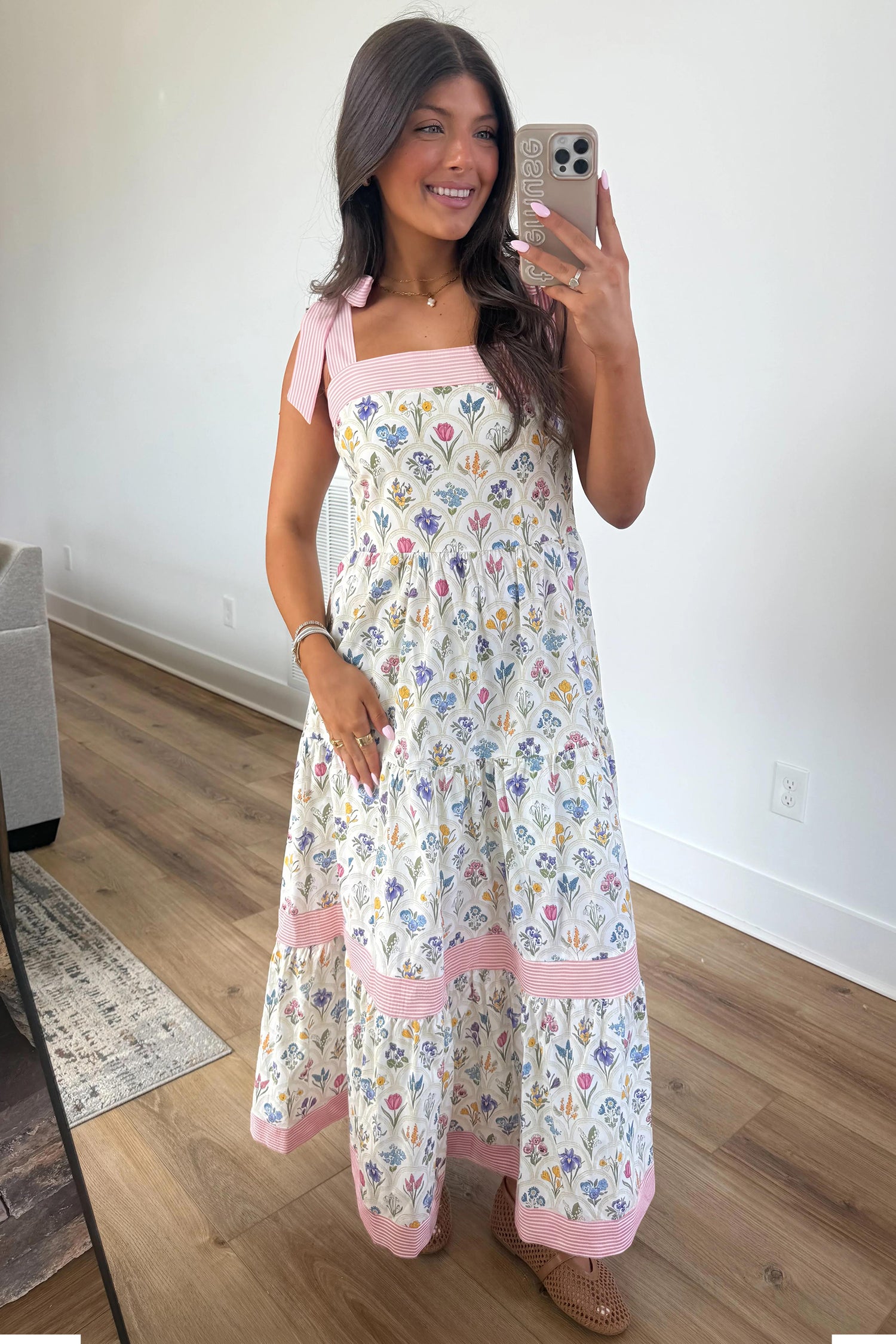 The Mia Dress floral maxi with pink striped straps, worn by a smiling woman; size chart lists S-M-L bust, waist, hem.